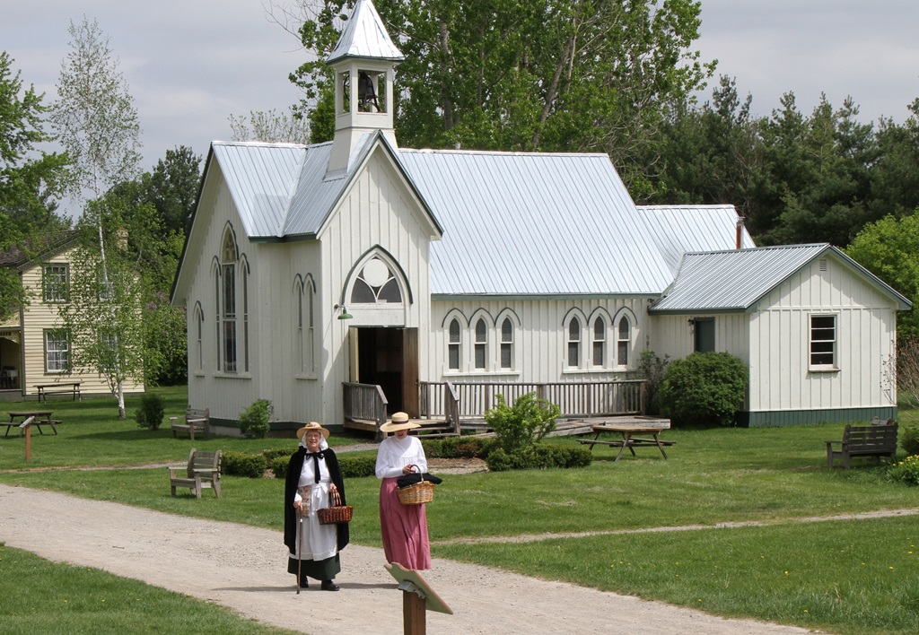 Two women walking on village path with white church in the background