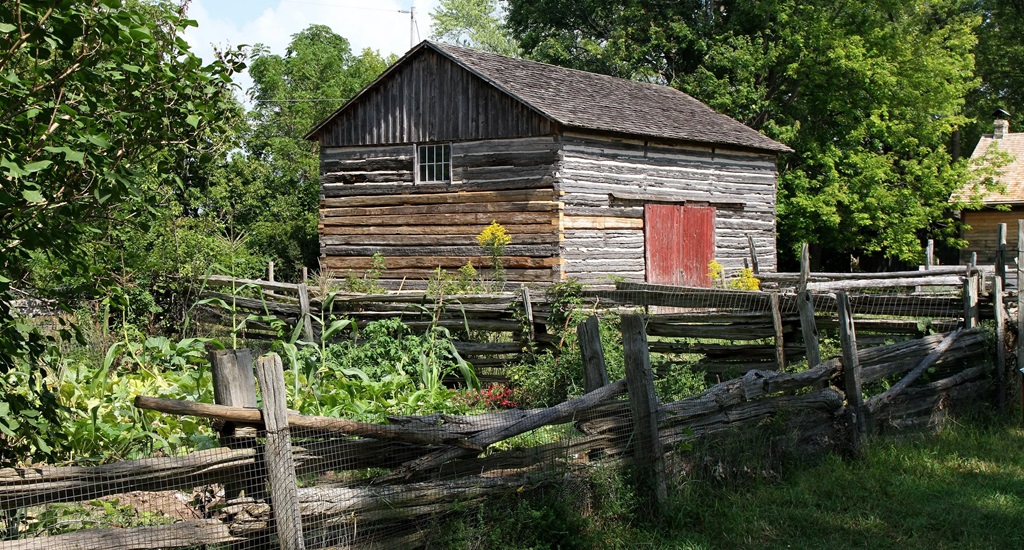 Pioneer garden with log building in the background - Fanshawe Pioneer Village